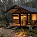 A modern expandable container cabin with wood siding and a black metal roof, glowing warmly in a lush, misty forest at dusk.